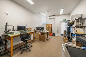 Office area featuring an AC wall unit, carpet floors, and vaulted ceiling