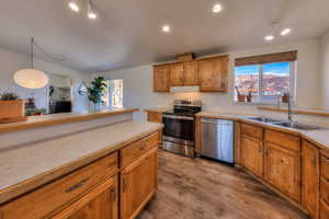 Kitchen with light wood-type flooring, stainless steel appliances, sink, decorative light fixtures, and lofted ceiling