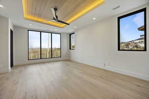 Empty room with ceiling fan, a raised ceiling, wooden ceiling, and light hardwood / wood-style flooring