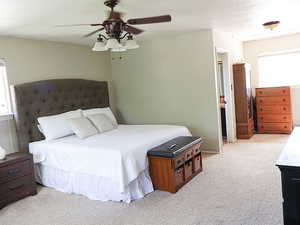 Bedroom with ceiling fan, light colored carpet, and a textured ceiling