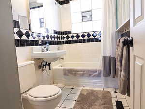 Full bathroom featuring shower / bath combo, sink, tile patterned flooring, toilet, and tile walls