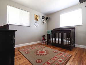 Bedroom featuring multiple windows, a crib, and hardwood / wood-style flooring