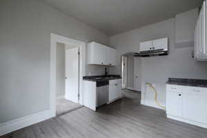 Kitchen featuring stainless steel dishwasher, light lvp floors, white cabinetry, and sink