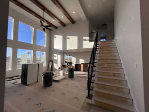 Stairs with beam ceiling, ceiling fan, and a towering ceiling