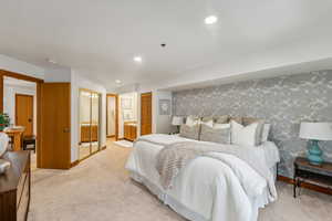 Bedroom featuring two closets, ensuite bathroom, and light colored carpet