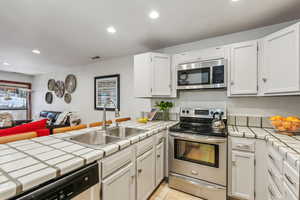 Kitchen featuring tile countertops, sink, white cabinets, and appliances with stainless steel finishes