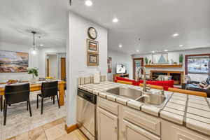 Kitchen with dishwasher, sink, hanging light fixtures, light tile patterned floors, and tile counters