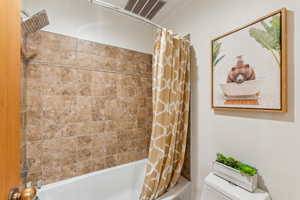 Bathroom featuring toilet and shower / bathtub combination with curtain