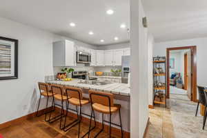 Kitchen with white cabinetry, sink, stainless steel appliances, tile countertops, and a kitchen bar