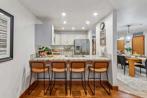 Kitchen featuring a kitchen breakfast bar, stainless steel fridge, tile counters, and white cabinets