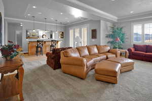 Carpeted living room with a textured ceiling, a wealth of natural light, crown molding, and indoor bar