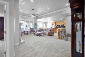 Living room with ceiling fan, crown molding, a textured ceiling, and light carpet