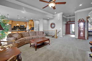 Carpeted living room with ceiling fan with notable chandelier and crown molding