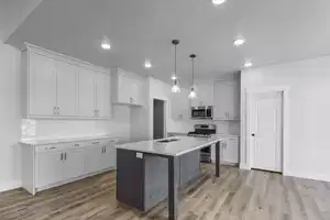 Kitchen with light wood-type flooring, a breakfast bar, stainless steel appliances, a kitchen island with sink, and decorative light fixtures