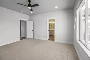 Unfurnished bedroom with multiple windows, light colored carpet, ensuite bath, and ceiling fan