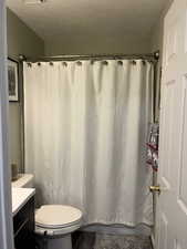 Bathroom with a shower with shower curtain, vanity, toilet, and a textured ceiling