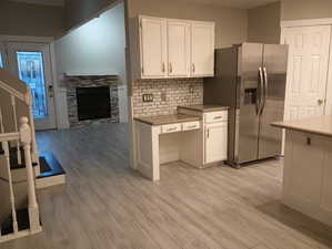 Kitchen with a stone fireplace, stainless steel refrigerator with ice dispenser, backsplash, light hardwood / wood-style floors, and white cabinets