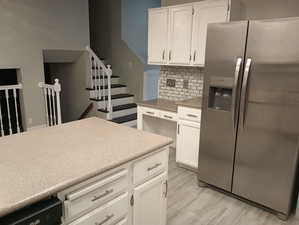 Kitchen with tasteful backsplash, white cabinetry, light hardwood / wood-style flooring, and stainless steel refrigerator with ice dispenser