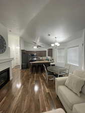 Living room featuring a textured ceiling, ceiling fan with notable chandelier, dark hardwood / wood-style floors, and lofted ceiling