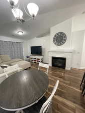 Living room featuring a textured ceiling, a notable chandelier, dark wood-type flooring, and vaulted ceiling