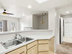 Kitchen featuring ceiling fan, sink, hanging light fixtures, light carpet, and light brown cabinetry