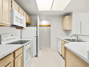 Kitchen with white appliances, sink, and light brown cabinetry