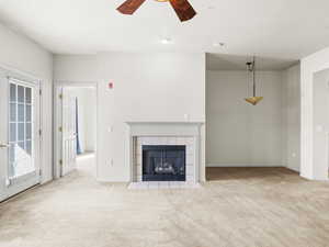 Unfurnished living room featuring light carpet, ceiling fan, and a tiled fireplace