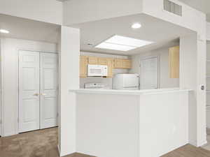 Kitchen featuring light colored carpet, white appliances, kitchen peninsula, and light brown cabinetry