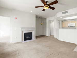 Unfurnished living room featuring ceiling fan, a fireplace, and light carpet