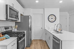 Kitchen with white cabinetry, sink, stainless steel appliances, kitchen peninsula, and light hardwood / wood-style floors