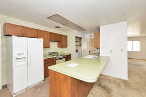 Kitchen with white refrigerator with ice dispenser, sink, stainless steel stove, separate washer and dryer, and kitchen peninsula