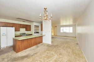 Kitchen with kitchen peninsula, light colored carpet, white fridge with ice dispenser, a chandelier, and hanging light fixtures