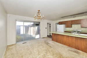 Kitchen with an inviting chandelier, white refrigerator with ice dispenser, kitchen peninsula, pendant lighting, and light colored carpet