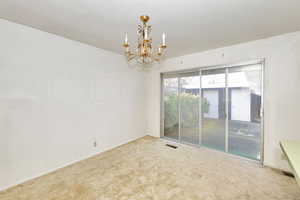 Carpeted empty room featuring an inviting chandelier