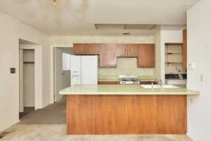 Kitchen with sink, white fridge with ice dispenser, kitchen peninsula, light colored carpet, and range