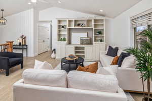 Living room featuring ceiling fan with notable chandelier, light wood-type flooring, and vaulted ceiling