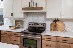 Kitchen with decorative backsplash, white cabinetry, and stainless steel electric stove