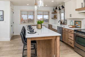 Kitchen featuring white cabinetry, a center island, light hardwood / wood-style floors, pendant lighting, and appliances with stainless steel finishes