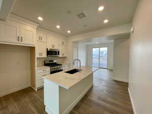 Kitchen with sink, appliances with stainless steel finishes, white cabinetry, light stone counters, and a center island with sink