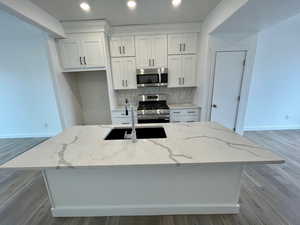 Kitchen with appliances with stainless steel finishes, a kitchen island with sink, sink, and white cabinets