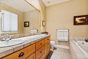 Bathroom with tile patterned floors, vanity, a relaxing tiled tub, and toilet