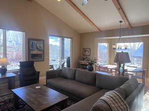 Living room with beam ceiling, ceiling fan with notable chandelier, and high vaulted ceiling