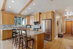 Kitchen with appliances with stainless steel finishes, a breakfast bar, vaulted ceiling with beams, light hardwood / wood-style floors, and a kitchen island