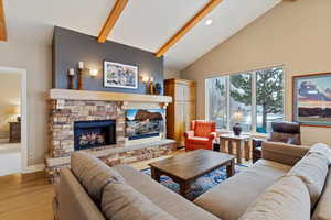 Living room with a stone fireplace, light hardwood / wood-style flooring, and lofted ceiling with beams