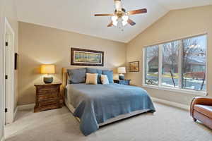 Carpeted bedroom featuring ceiling fan, vaulted ceiling, and multiple windows