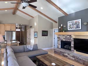 Living room with beamed ceiling, high vaulted ceiling, ceiling fan, and a stone fireplace