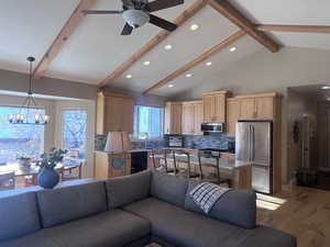 Living room with vaulted ceiling with beams, light hardwood / wood-style flooring, and ceiling fan with notable chandelier