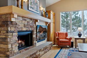 Living area with a stone fireplace, light hardwood / wood-style floors, and vaulted ceiling