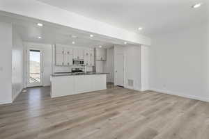 Kitchen with stainless steel appliances, decorative backsplash, a center island with sink, white cabinets, and light wood-type flooring