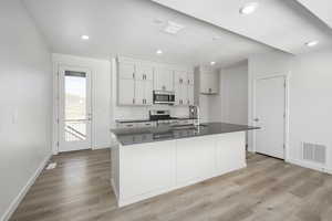 Kitchen with stainless steel appliances, a kitchen island with sink, sink, light hardwood / wood-style flooring, and white cabinets